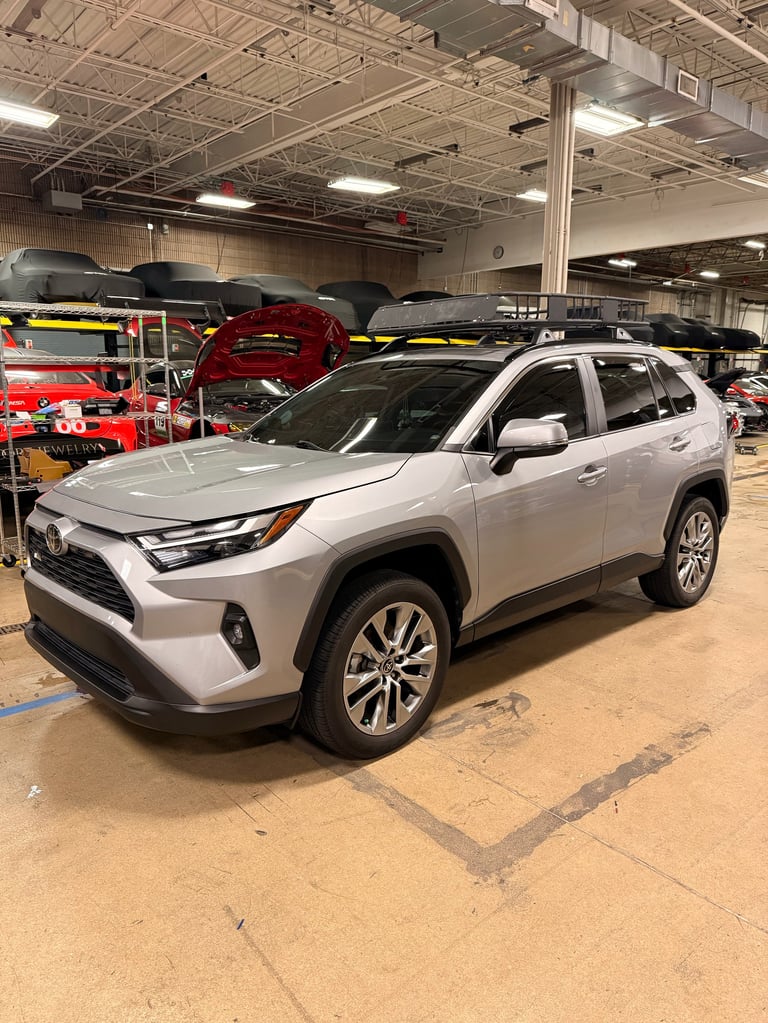 Silver Toyota RAV4 SUV on display in an indoor warehouse with red vehicles and industrial lighting visible in background