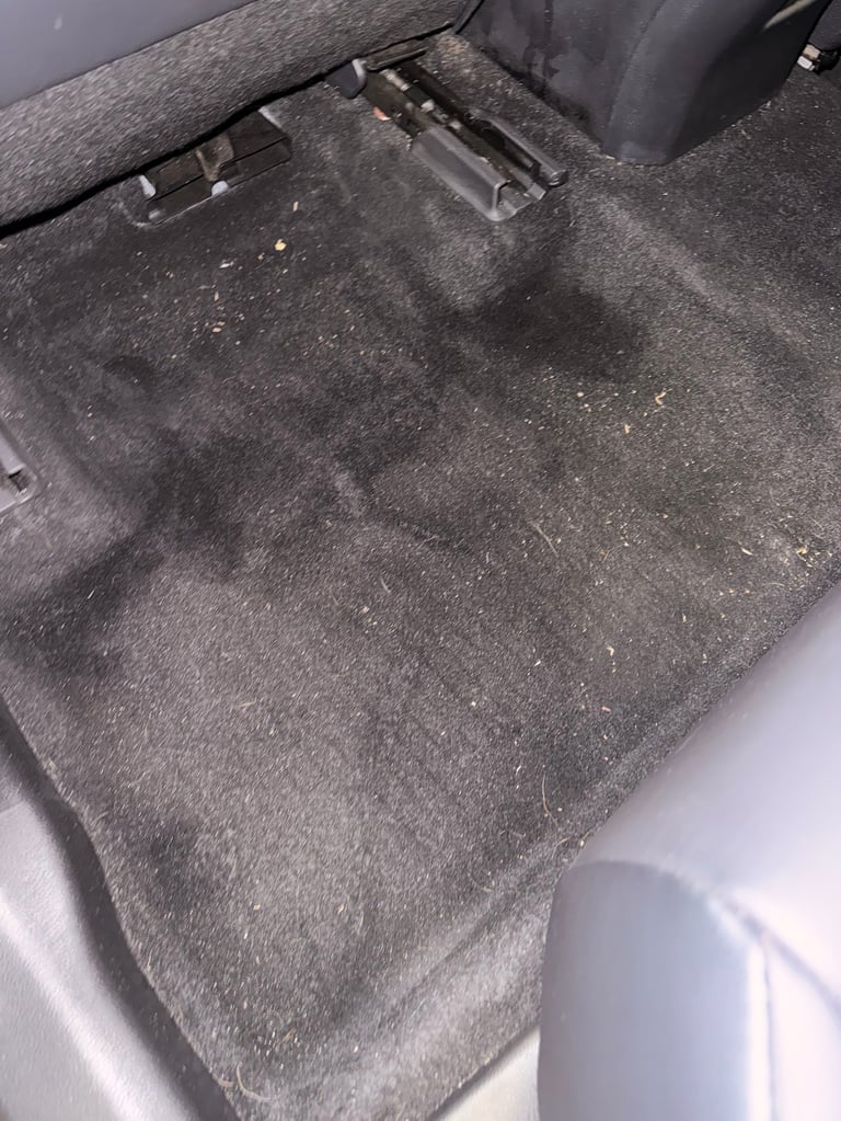 Close-up of dirty car interior floor mat with visible stains and debris scattered across gray carpet