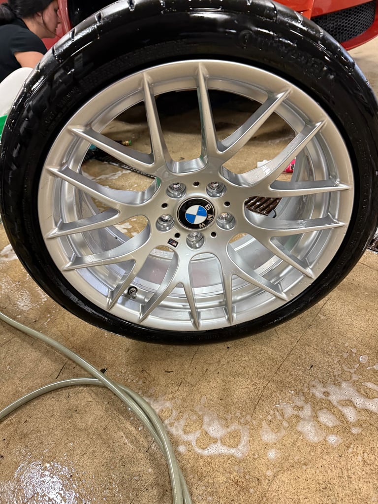 Silver BMW alloy wheel with black tire being displayed at an automotive event or car show
