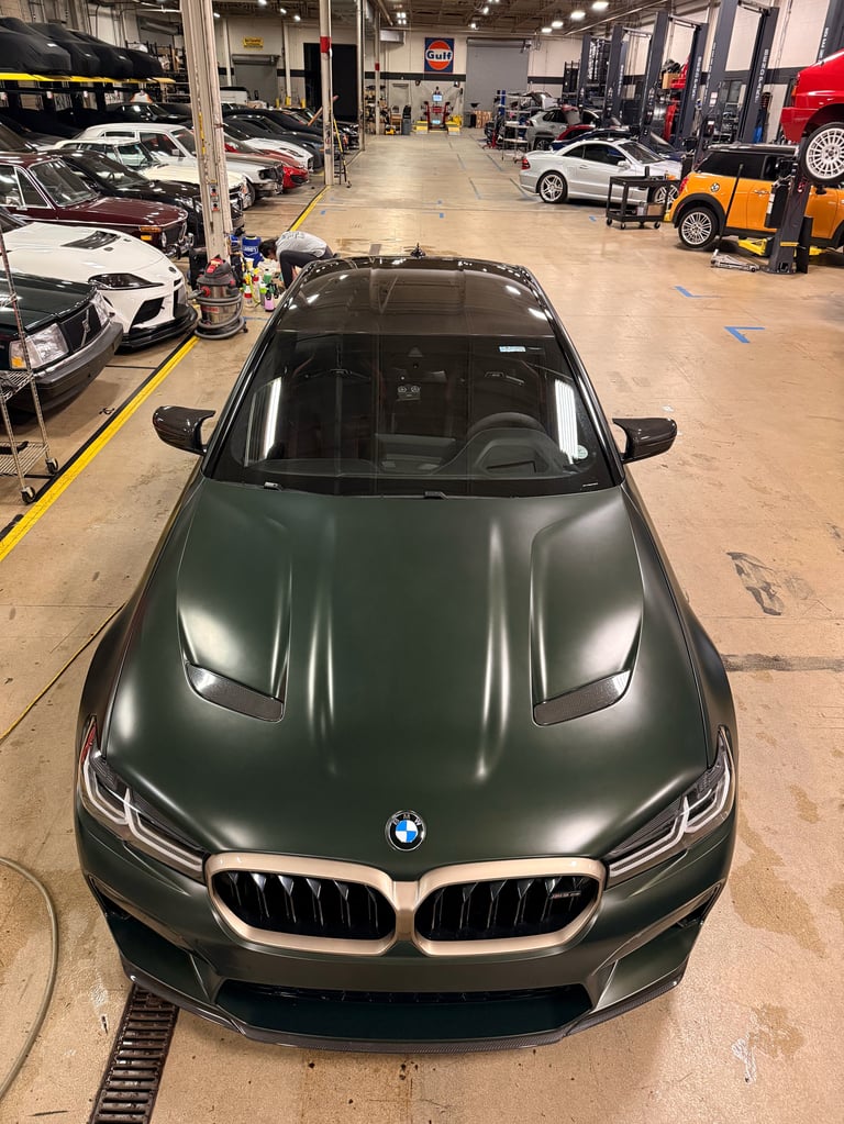 Dark green BMW sedan parked inside an automotive service facility with other cars and equipment visible in the background
