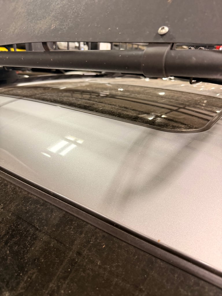 Close-up of white vehicle roof with black roof rack and tinted skylight window