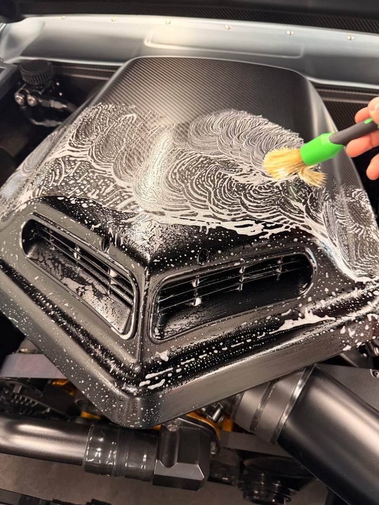 Person cleaning car engine intake manifold with soap and brush during vehicle maintenance
