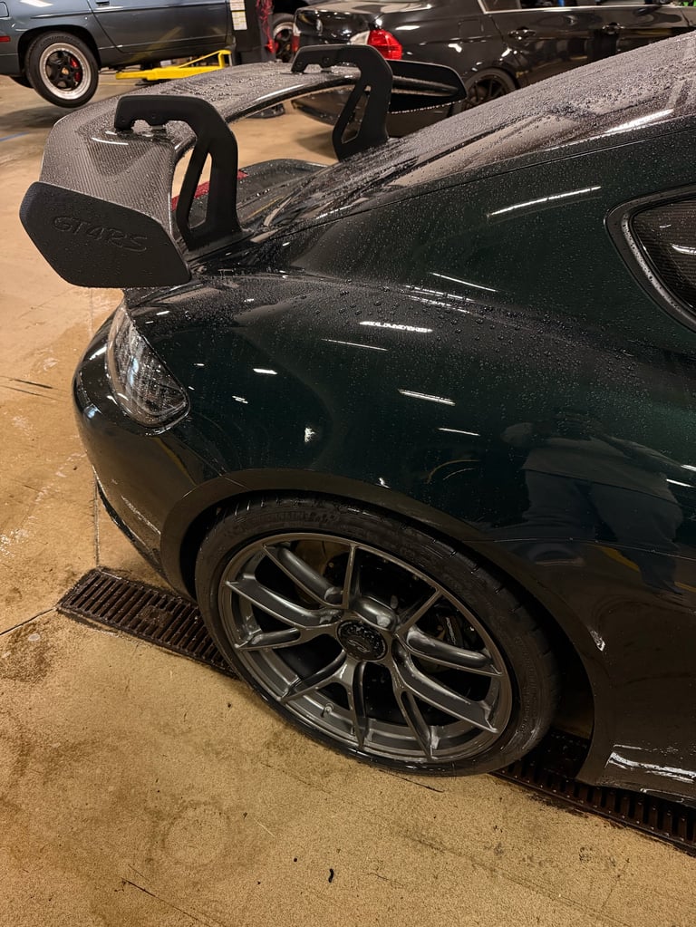 Black sports car with open hood at indoor car show, displaying engine compartment with vintage vehicles in background