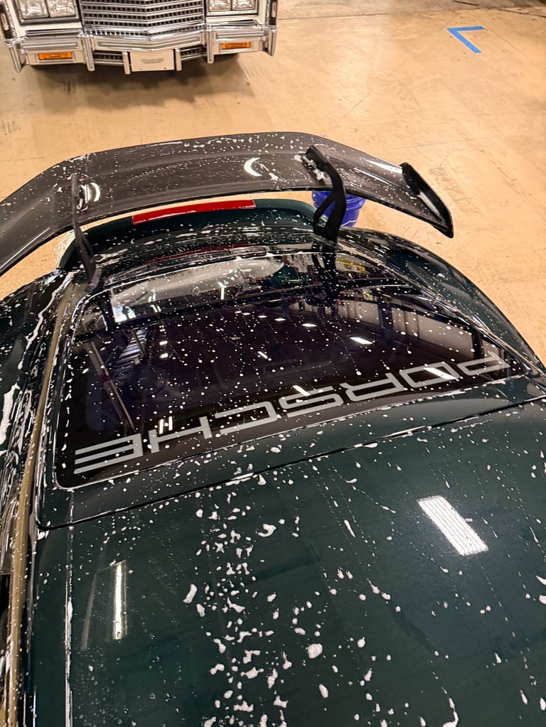 Dark green car with aerodynamic roof spoiler covered in water droplets in outdoor lot