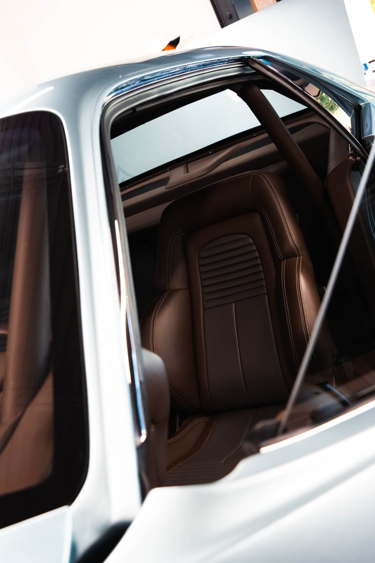 White vintage car interior with brown leather seats and open door, viewed from above at an angle