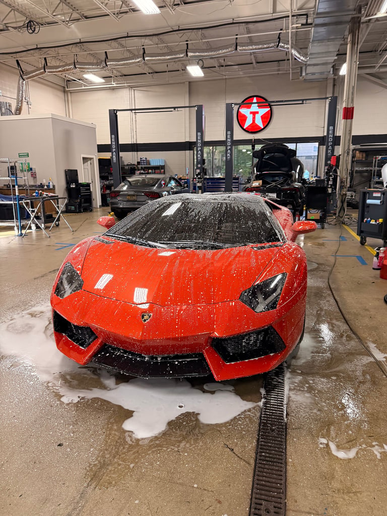 Red Lamborghini being washed in an automotive service garage with industrial ceiling and equipment