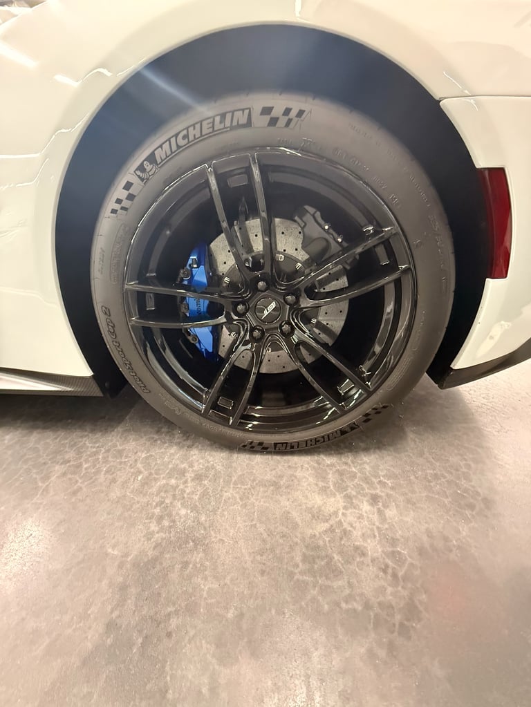 Close-up of a white cars wheel with a black Michelin tire and dark multi-spoke alloy rim with blue brake calipers visible