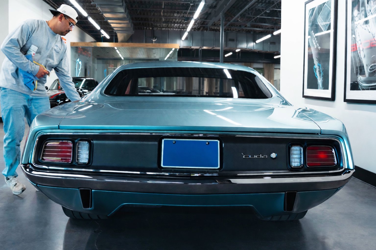 Mechanic in blue uniform working on the engine of a turquoise classic car in a modern automotive workshop