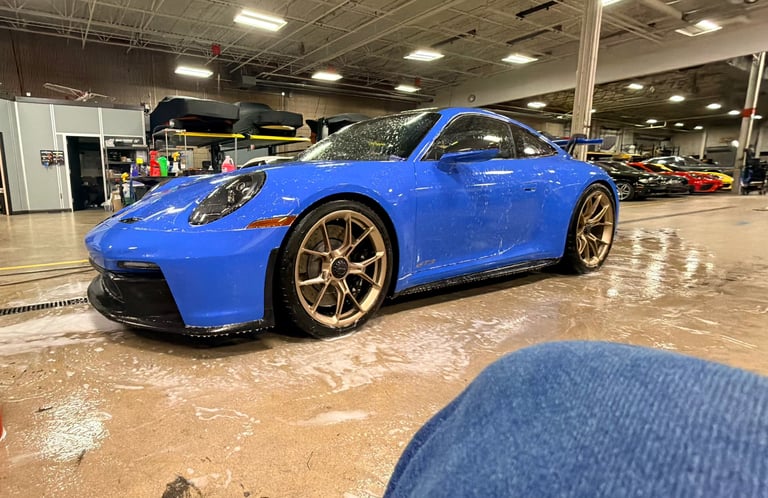 Blue Porsche sports car with gold wheels displayed in an indoor garage showroom