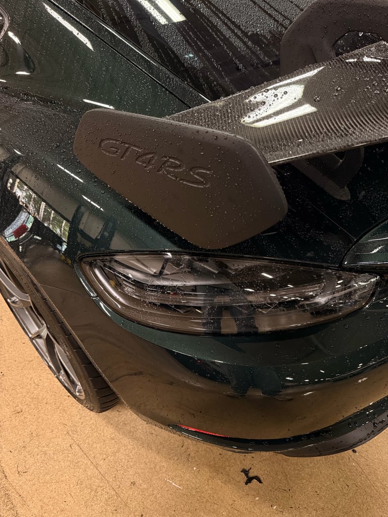 Close-up of a dark green Ford GT sports car front bumper and headlight assembly on concrete