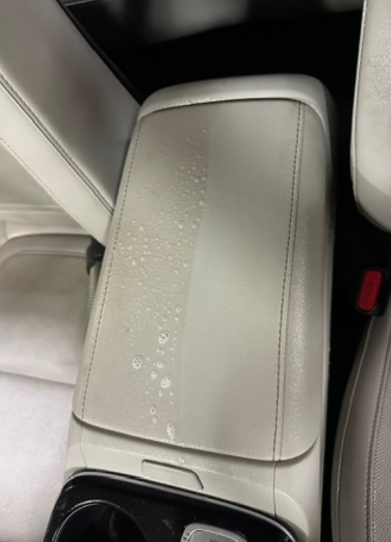 Water droplets on white leather car center console armrest in vehicle interior
