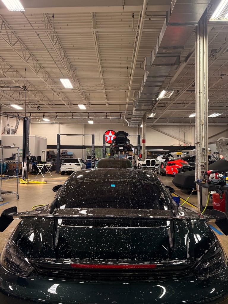 Black vehicle in automotive service garage with lift equipment and workshop tools visible