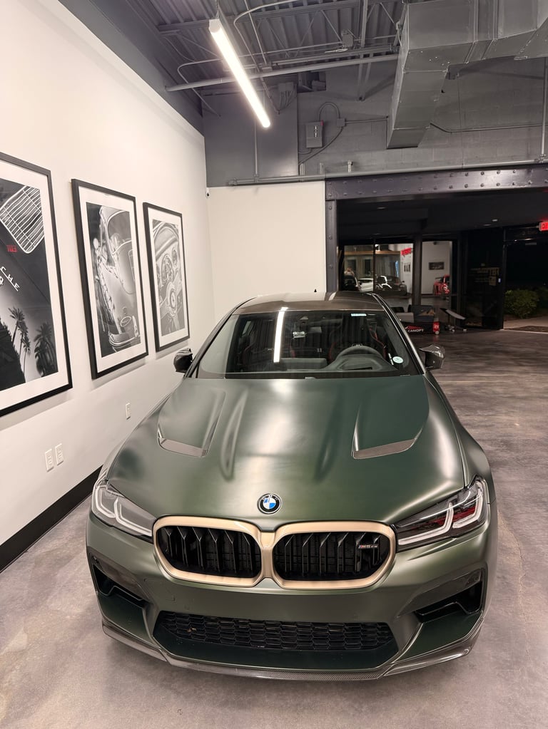 Green BMW M sport sedan displayed in an indoor showroom with white walls and framed artwork