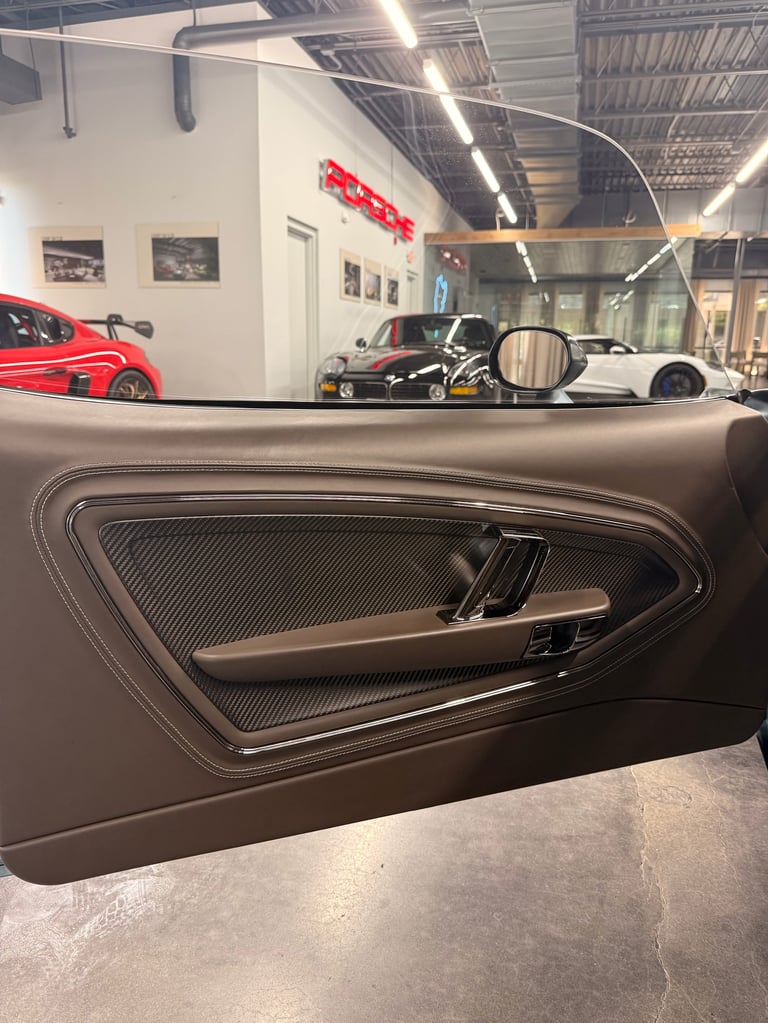 Interior car door panel with metal handle in a showroom displaying sports cars and signage