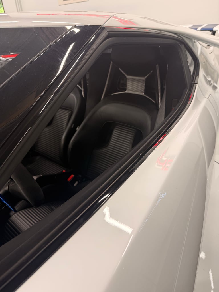 Interior view of a sports car showing black racing seats and steering wheel through the open driver door