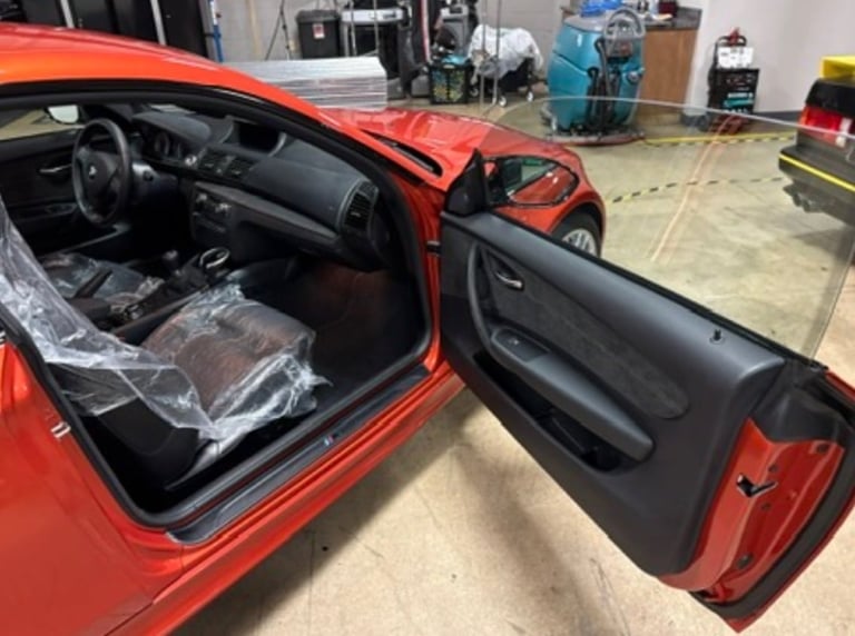 Red convertible car with drivers door open in an automotive workshop, showing black interior and exposed top