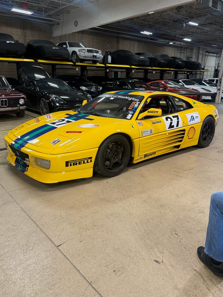 Yellow Ferrari 348 race car with number 27 displayed in an indoor garage with other vehicles