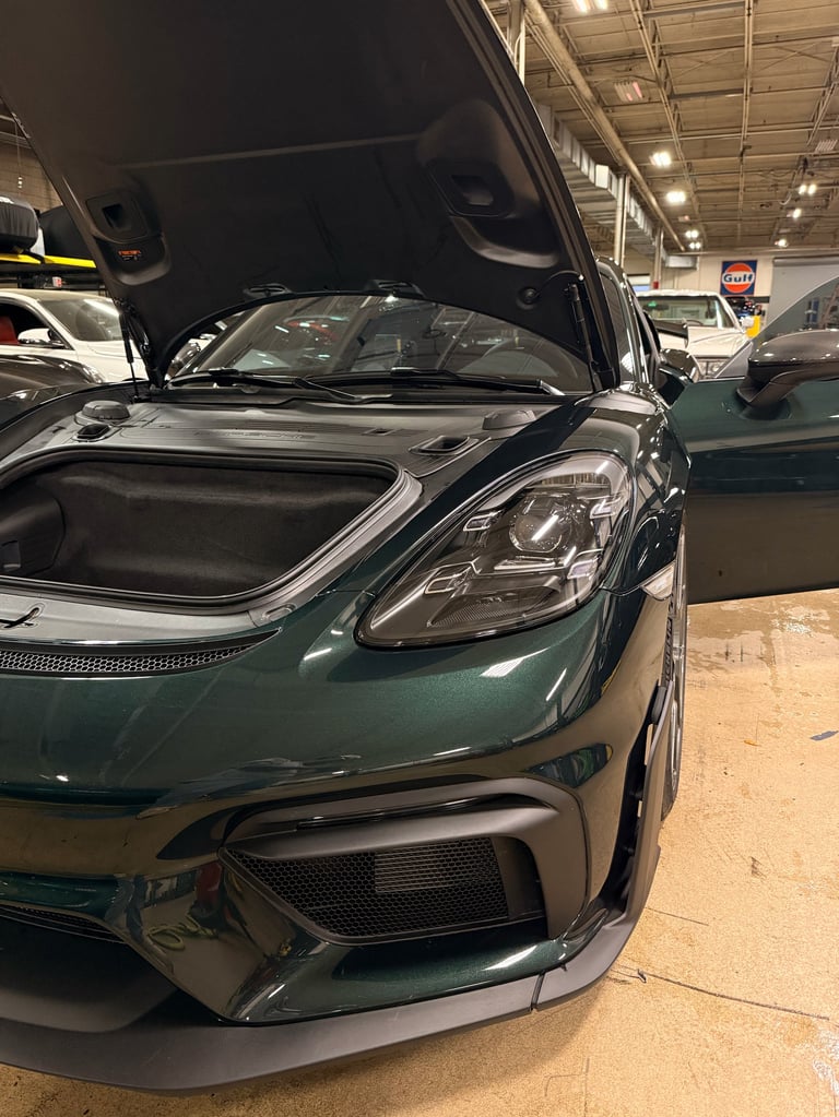 Green sports car with open hood displayed in warehouse showroom, other vehicles visible in background