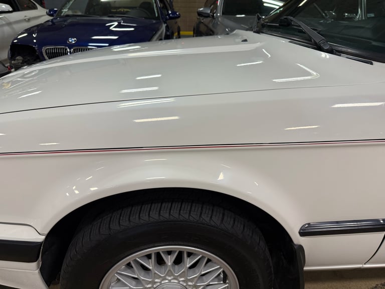 Close-up of white classic car hood and wheel at dealership, showing sleek bodywork and chrome trim details