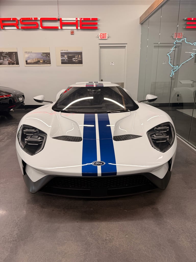 White Ford GT supercar with blue racing stripes displayed in a showroom with red neon signage