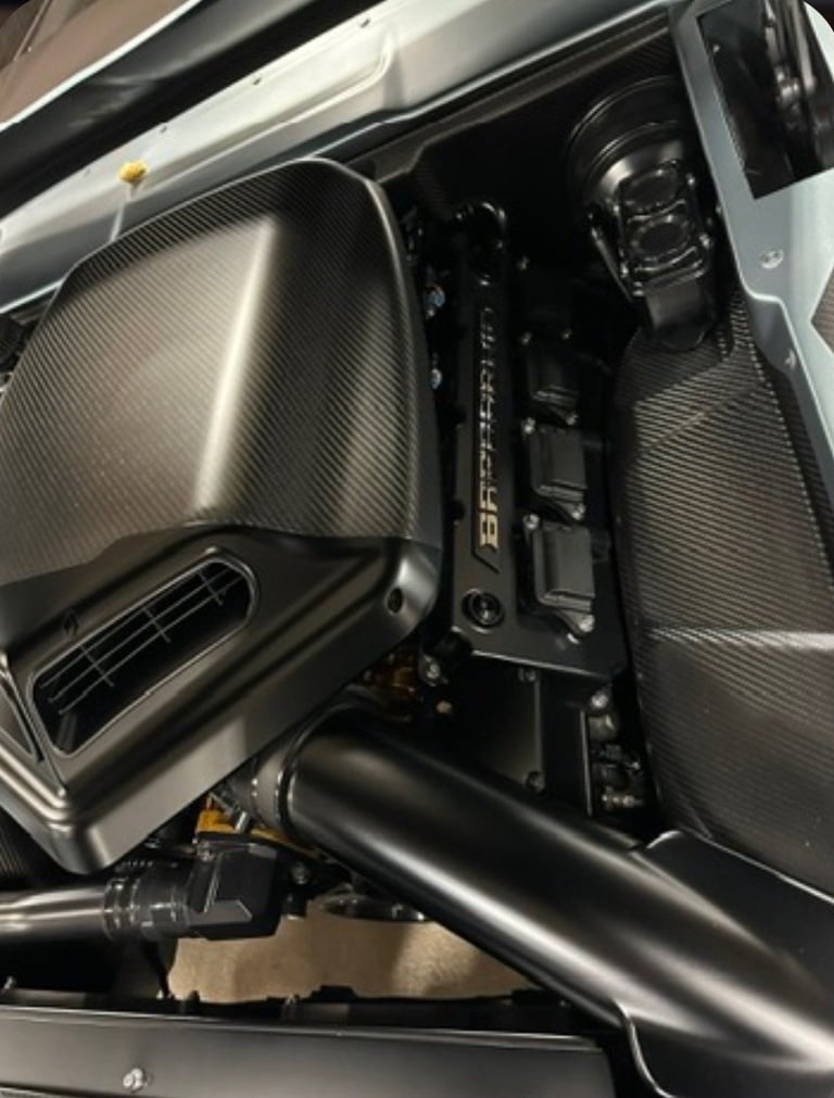 Car engine bay with carbon fiber intake manifold and components visible from overhead view