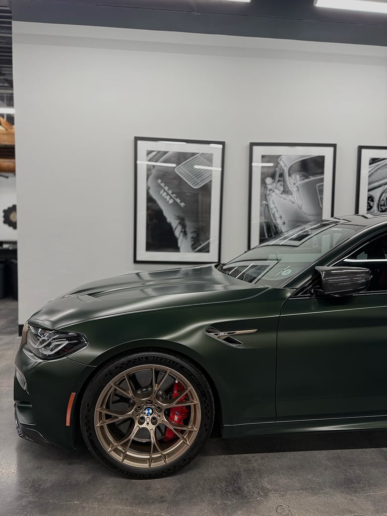 Green BMW sports car displayed in showroom with framed black and white automotive photographs on white wall behind it