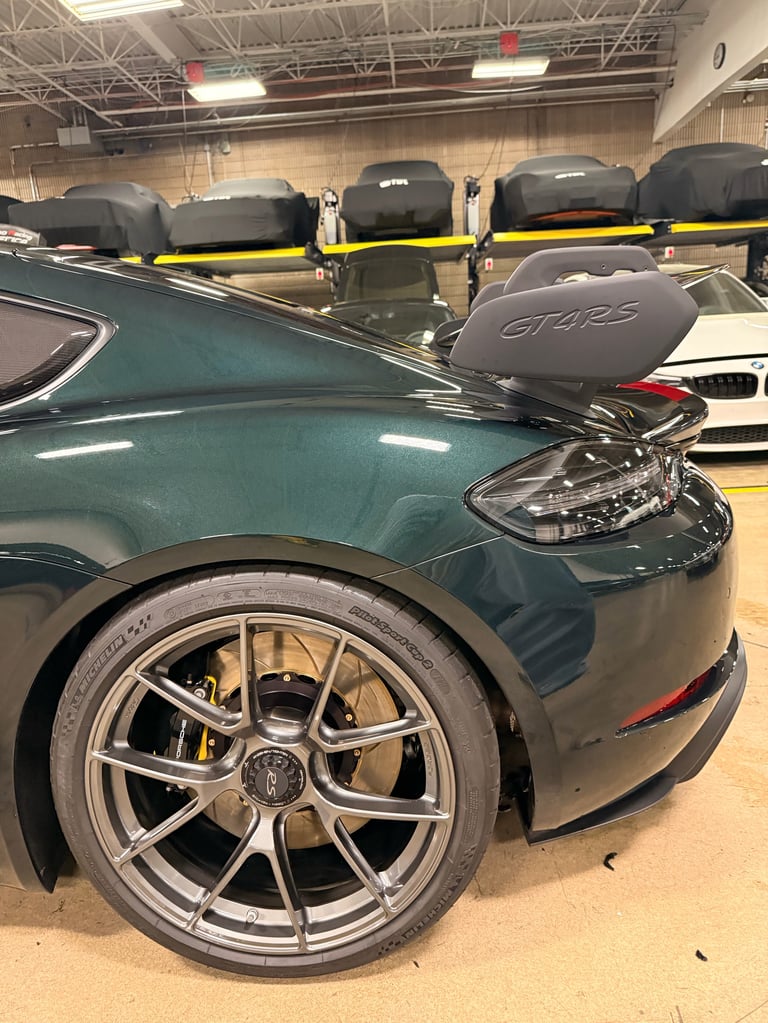 Dark teal sports car with roof rack in indoor warehouse garage with other vehicles parked behind