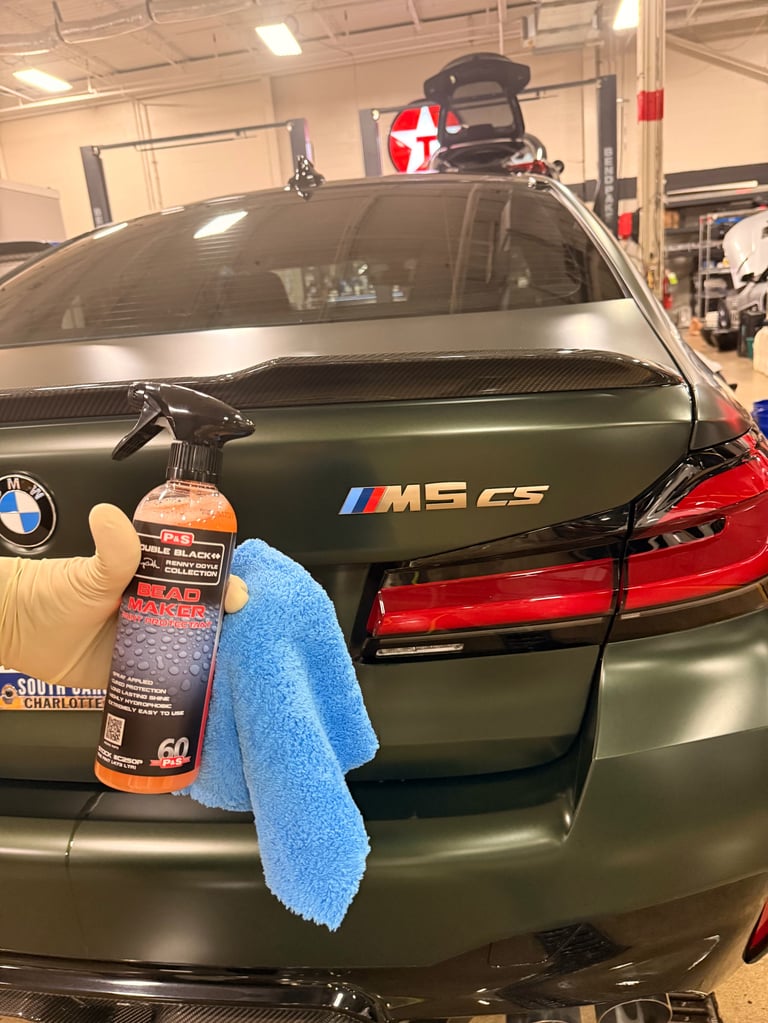 Green BMW M5 G5 car being detailed with cleaning spray and microfiber cloth in an indoor garage