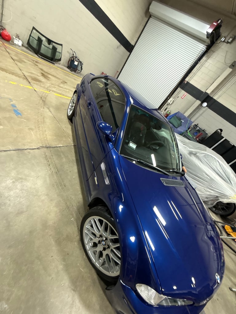 Blue car parked in an industrial garage or warehouse facility with concrete floor and metal rollup door