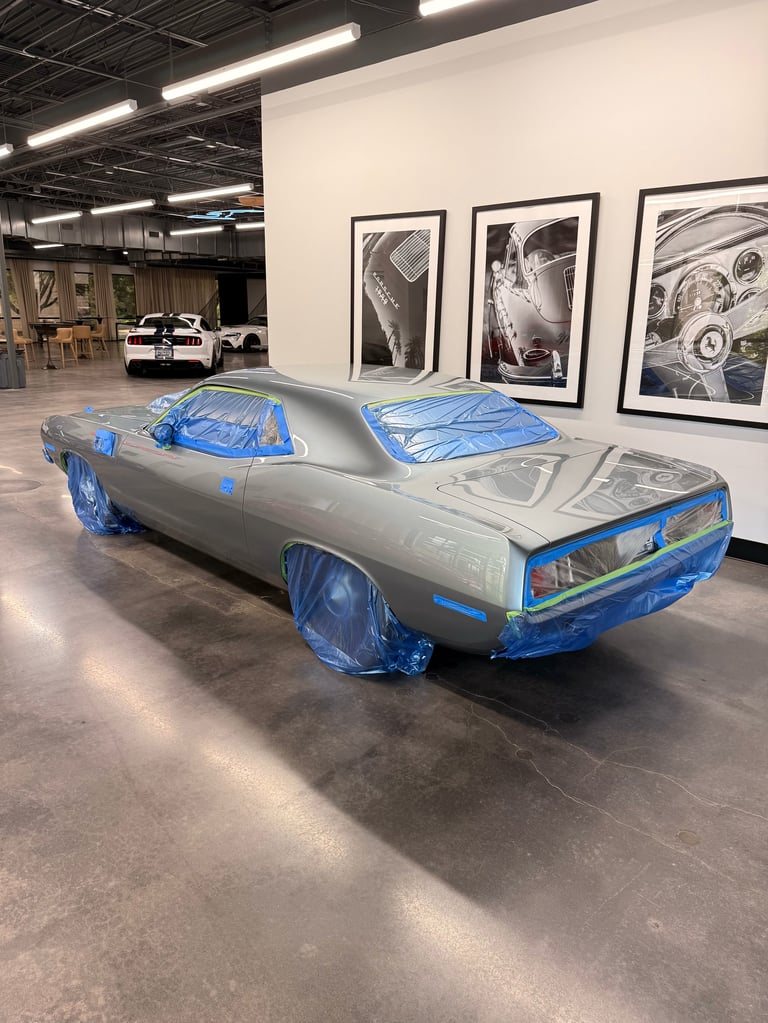 Silver vintage muscle car covered in blue plastic wrap in an automotive workshop with black and white photos on the wall
