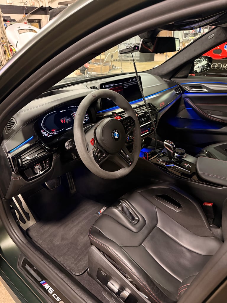 BMW M5 interior with steering wheel, digital dashboard, blue accents, and gray leather seats viewed from drivers door