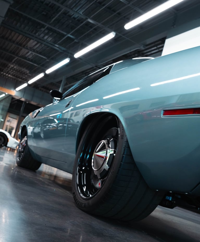 Light blue vintage car with open hood displayed in modern garage with industrial ceiling and fluorescent lighting