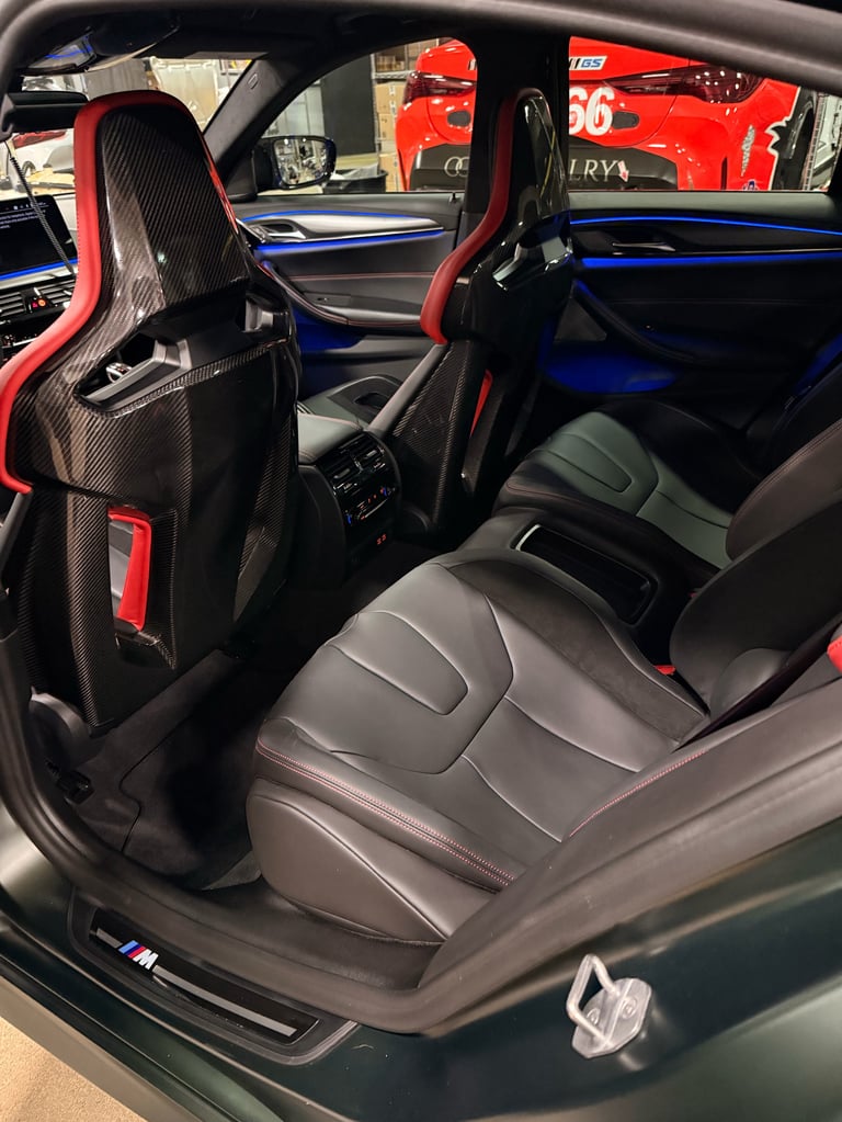 Interior of a sports car with red and black carbon fiber racing seats, blue trim accents, and a red Ferrari visible outside through the window