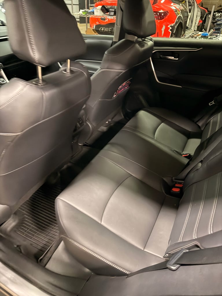 Interior view of a vehicle showing gray leather seats with white stitching and a black back seat, garage setting visible