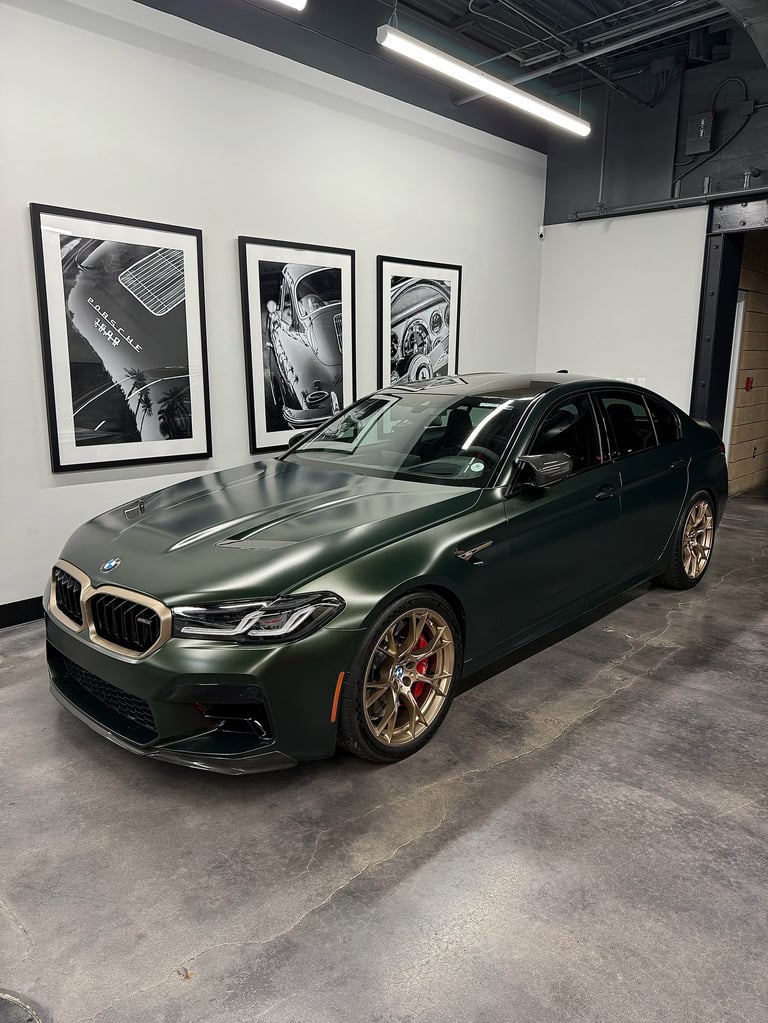 Dark green BMW M340i sedan displayed in a modern showroom with black and white automotive photography on the walls