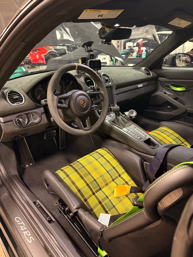 Interior of Porsche 911 GT3 with black leather seats, yellow racing straps, steering wheel, and dashboard visible through windshield