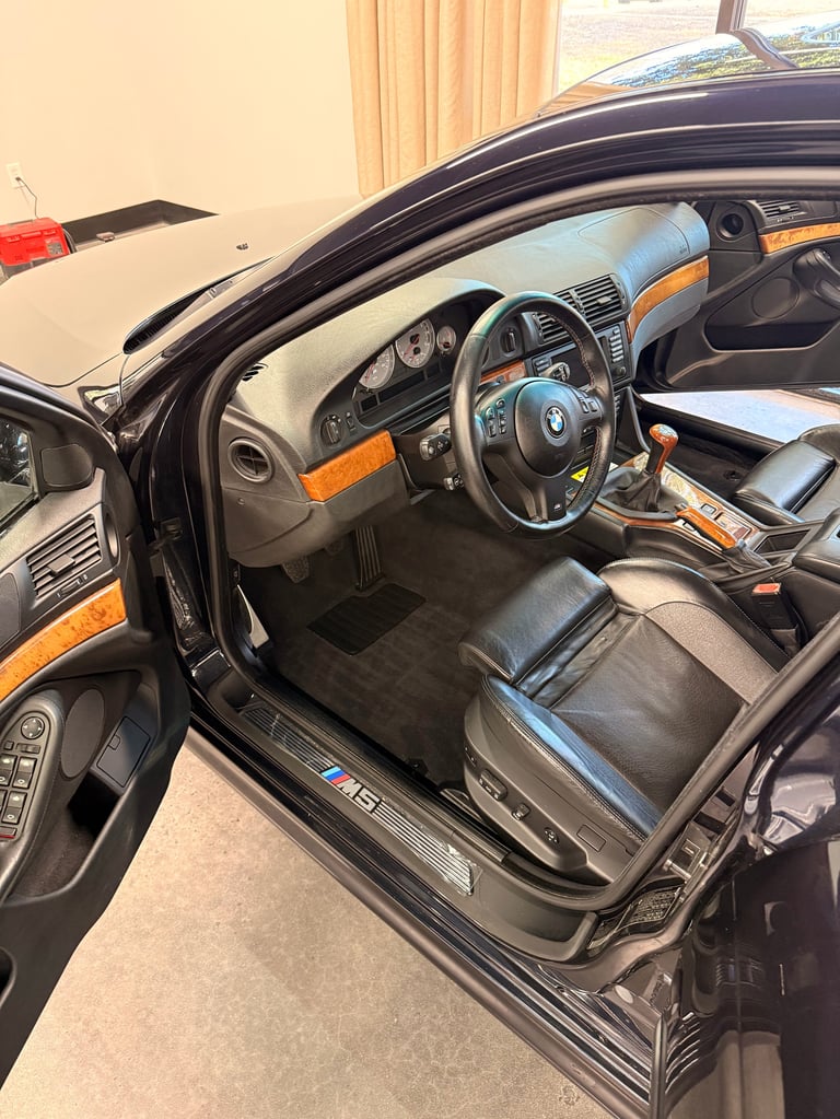 Interior of black BMW with orange and black leather seats, steering wheel, and dashboard trim visible through open driver door