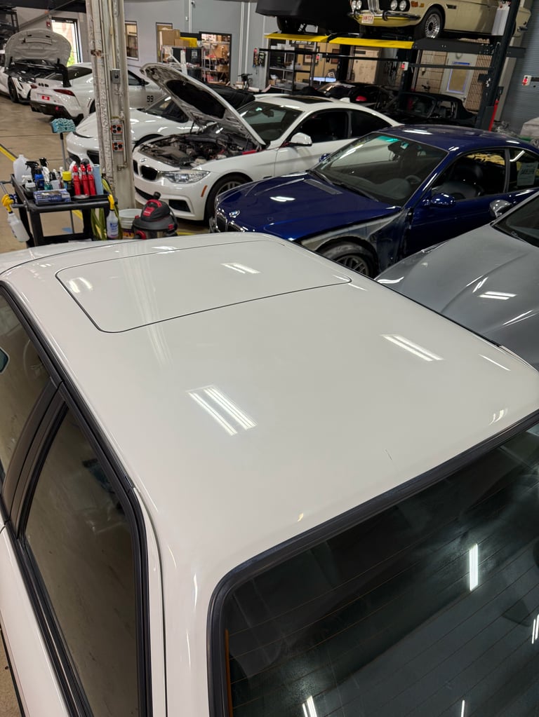 White car with open hood in auto repair shop with multiple vehicles and service equipment visible