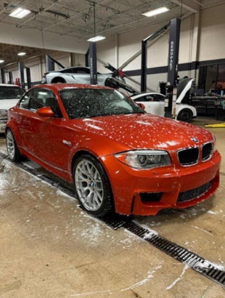 Red BMW 1-Series coupe in an auto repair garage with lift equipment visible in the background