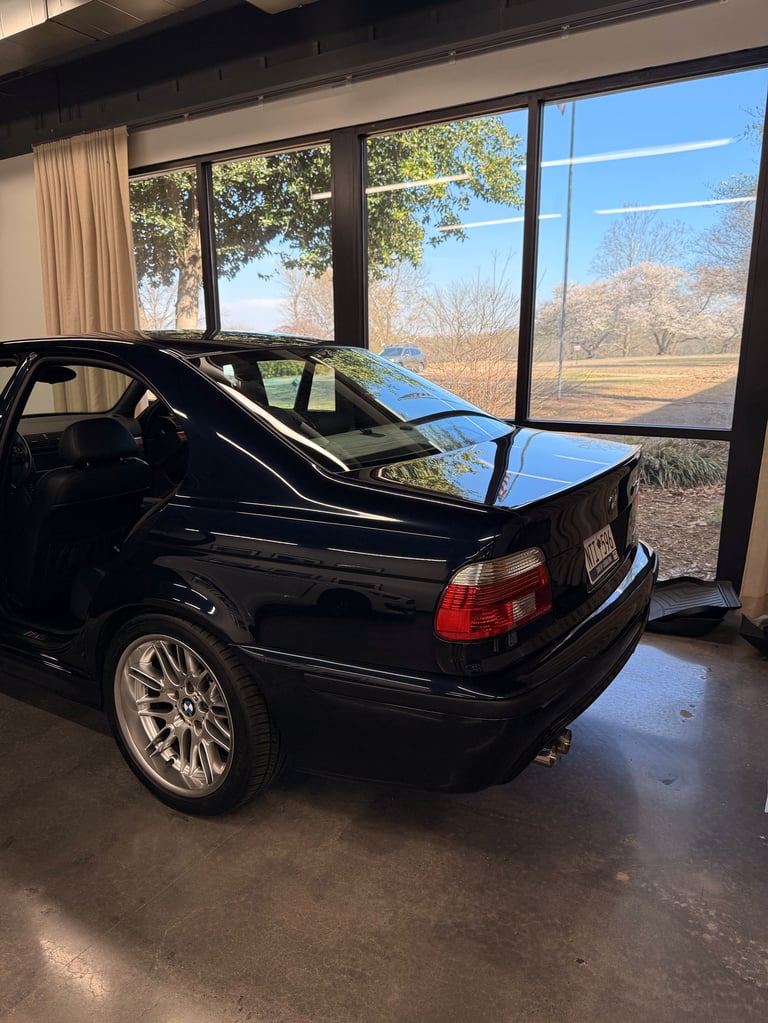 Black sedan with open trunk displayed in a showroom with large windows overlooking autumn landscape