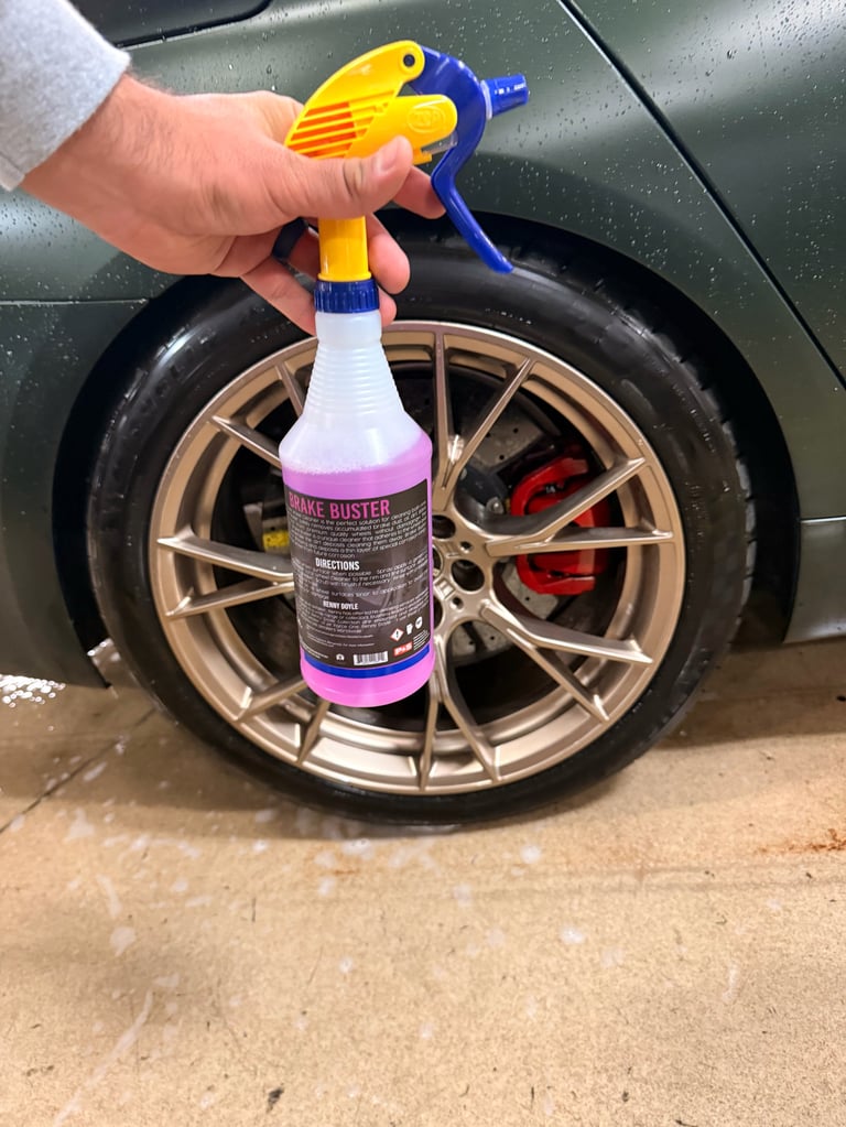 Person holding a spray bottle with yellow and blue trigger sprayer next to a car wheel for cleaning