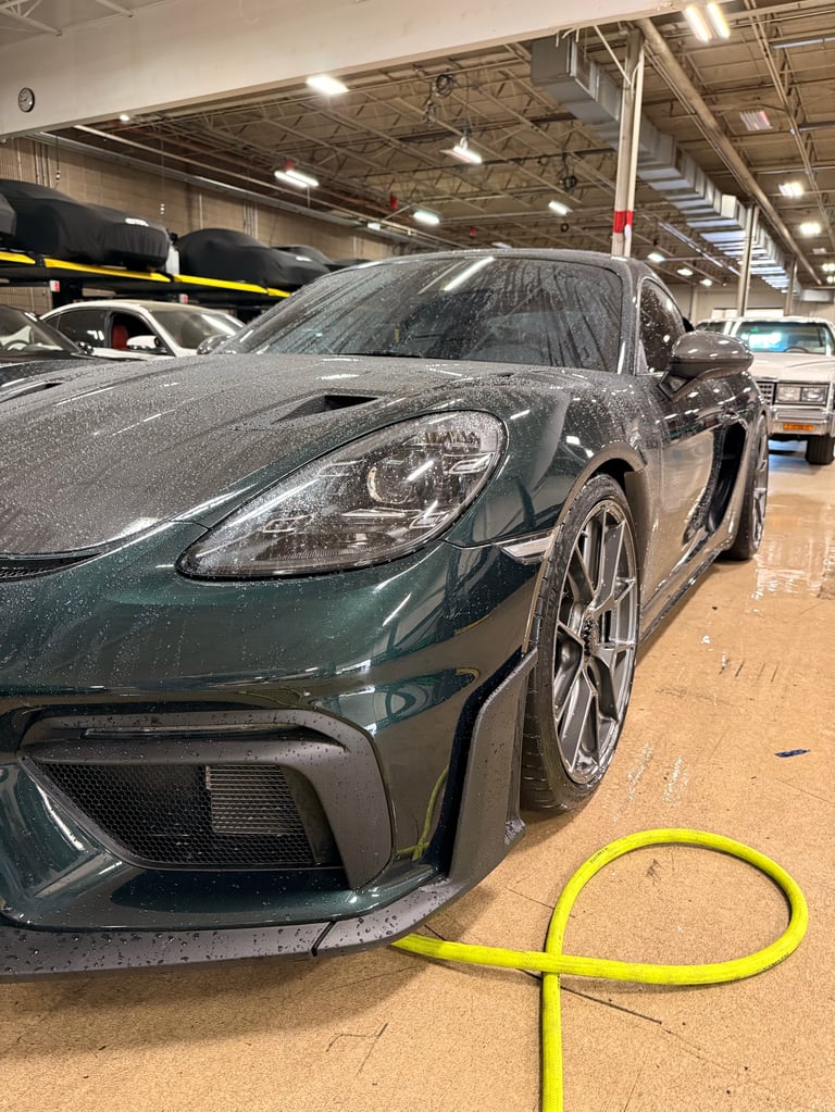 Dark green sports car in an industrial garage with a yellow cable in the foreground