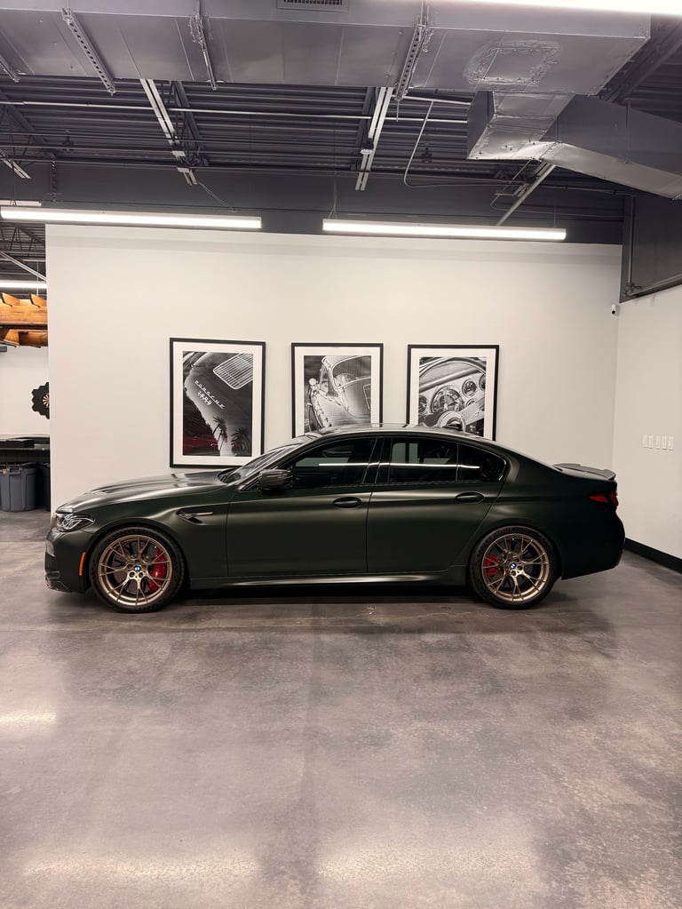 Dark green high-performance sedan displayed in a modern garage with black and white framed car artwork on the wall