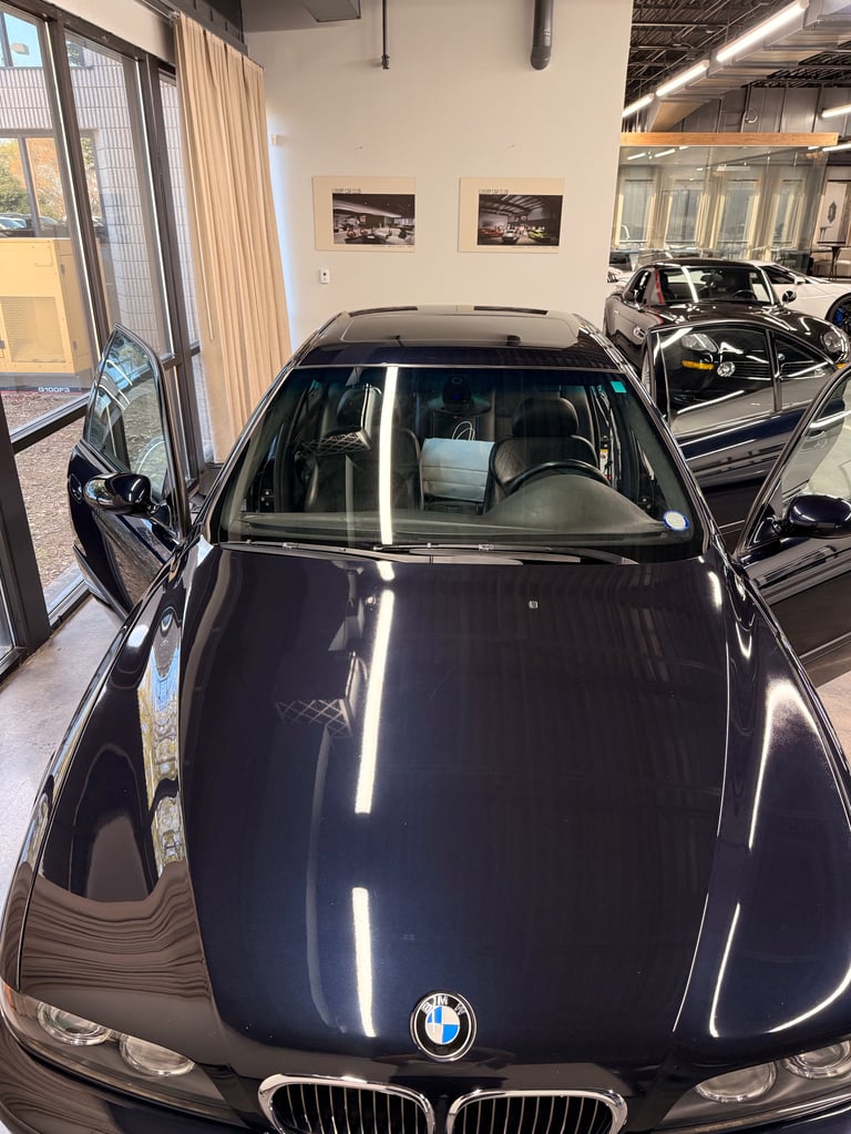 Black BMW car displayed in an indoor showroom with windows and other vehicles visible in the background