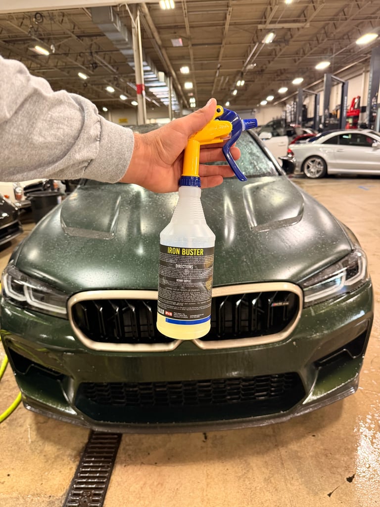Person holding cleaning spray bottle over hood of green BMW in car wash facility