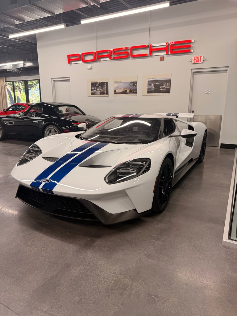 White sports car with blue racing stripes in Porsche dealership showroom