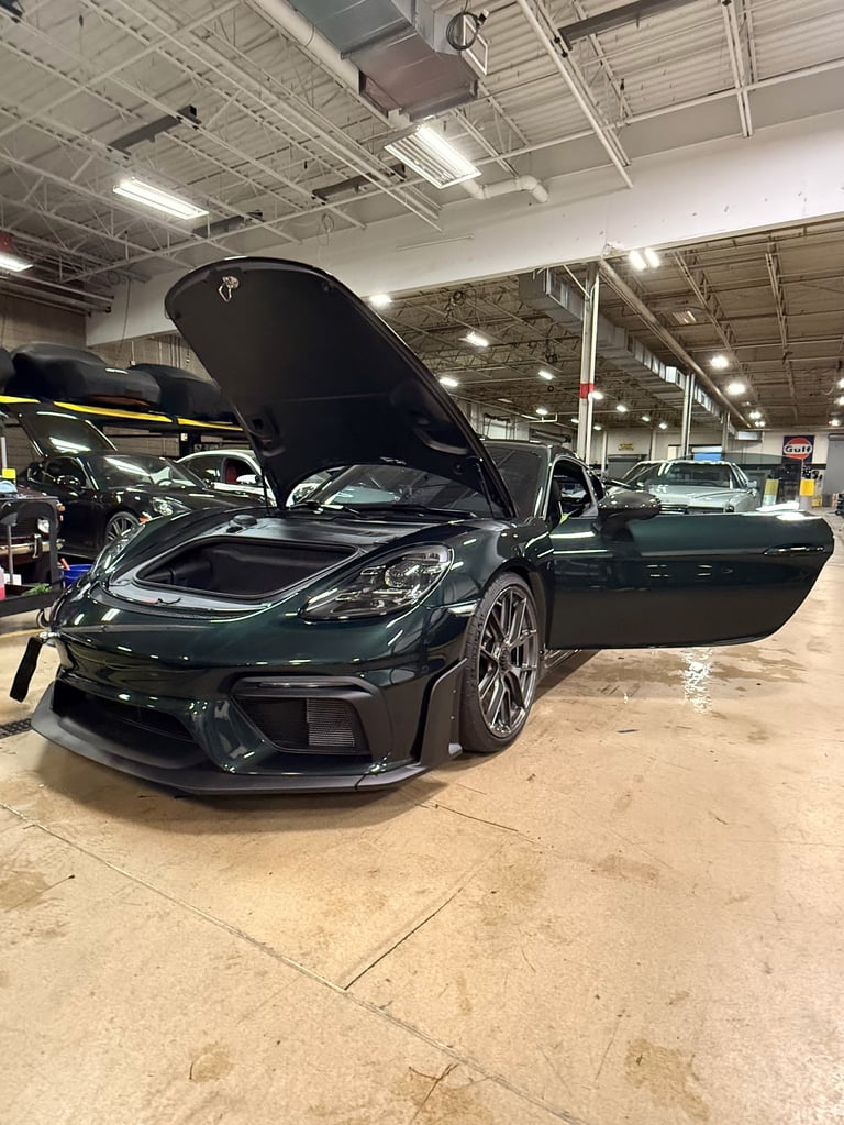 Dark green sports car with open hood in warehouse garage, with other vehicles visible in background