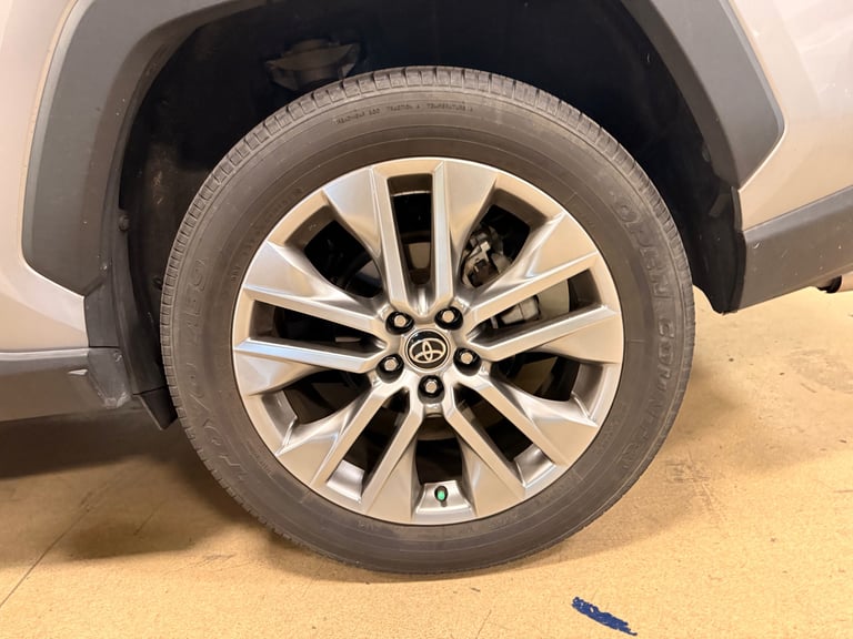 Close-up of a silver and black alloy wheel on a vehicle, mounted on a tire, parked on a sandy surface