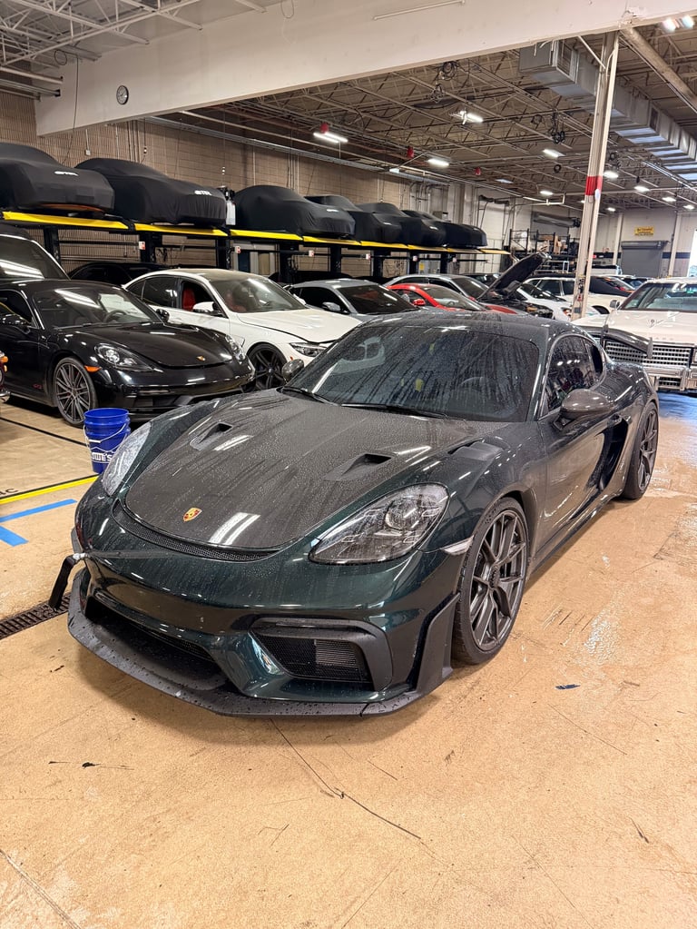 Black Porsche sports car on display in a warehouse showroom with multiple vehicles and roof racks visible in background