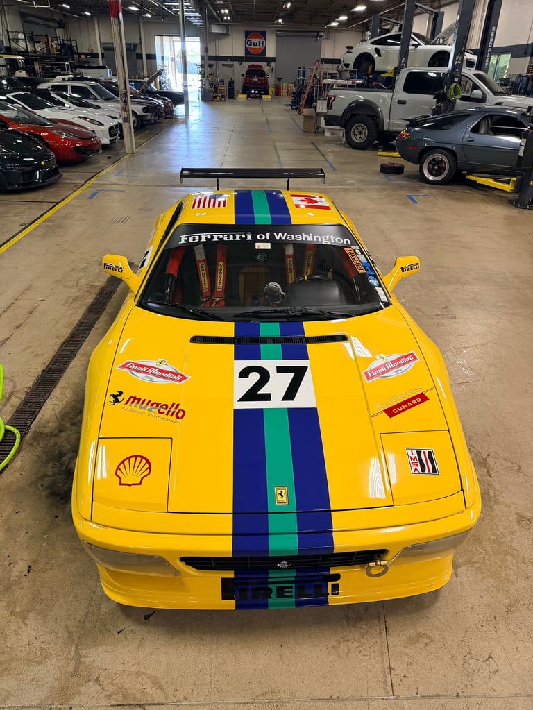 Yellow Ferrari race car with blue and green racing stripes and number 27 in a car workshop garage
